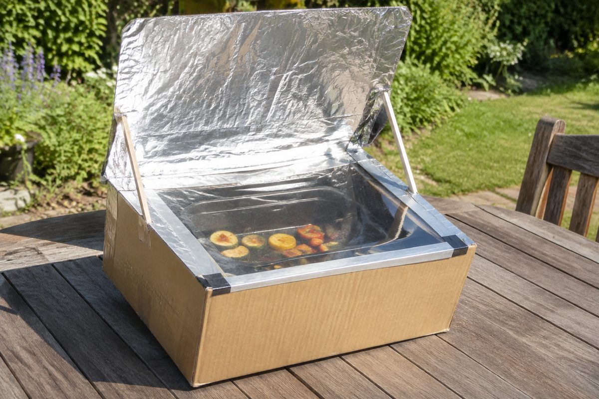 Four solaire en carton avec rabat réflecteur en papier aluminium posé sur une table en bois dans un jardin ensoleillé